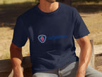 Seated on a wooden bench outdoors, a person wears a navy T-shirt featuring the iconic Scania logo and emblem from Garment Graphics. A lush, grassy area in the blurred background adds to the serene setting.