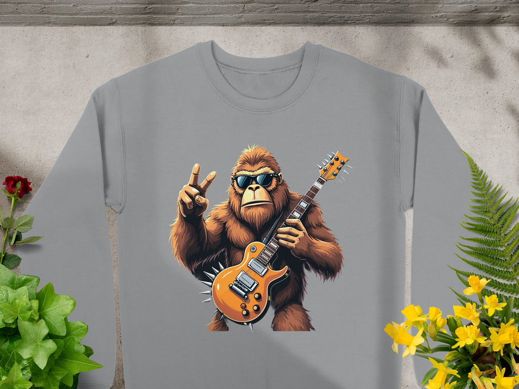 Garment Graphics gray sweatshirt showcases a gorilla in sunglasses, rocking an electric guitar and a peace sign. Its placed on concrete with green leaves and yellow flowers, ideal for music enthusiasts.