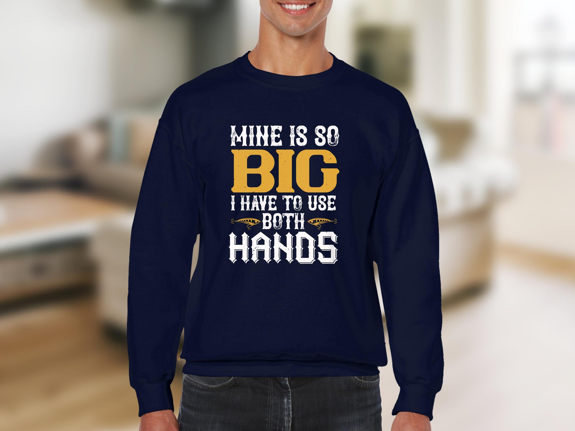 A person wears a Garment Graphics navy blue sweatshirt with the playful slogan Mine Is So Big I Have To Use Both Hands in white and yellow. The background shows a softly blurred living room, enhancing the sweatshirts unique design.