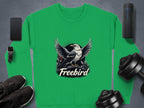 The Garment Graphics Freebird Graphic Sweatshirt, featuring an eagle with outstretched wings, is styled on a grey surface alongside a smartphone, wireless speaker, smartwatch, headphones, and dumbbells. It offers unisex sizing for the perfect fit.
