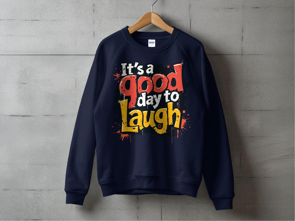 A navy blue, unisex sweatshirt from Garment Graphics hangs on a wooden hanger against a concrete wall. It features bold, colorful text reading Its a Good Day to Laugh.