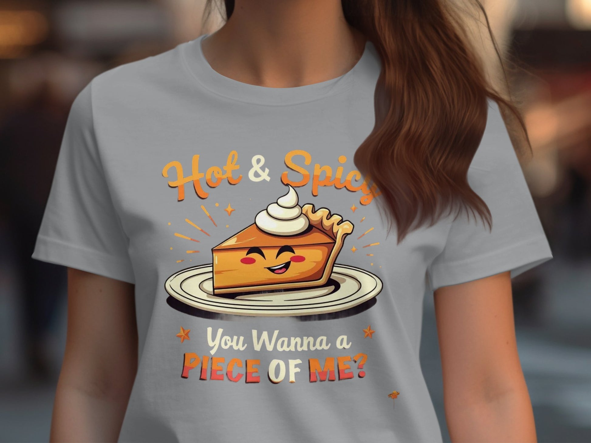 A woman wears a Garment Graphics gray t-shirt showcasing a pie slice with whipped cream. Hot & Spicy is above the image and You Wanna a Piece of Me? below. Ideal for casual outings, the background is creatively blurred.