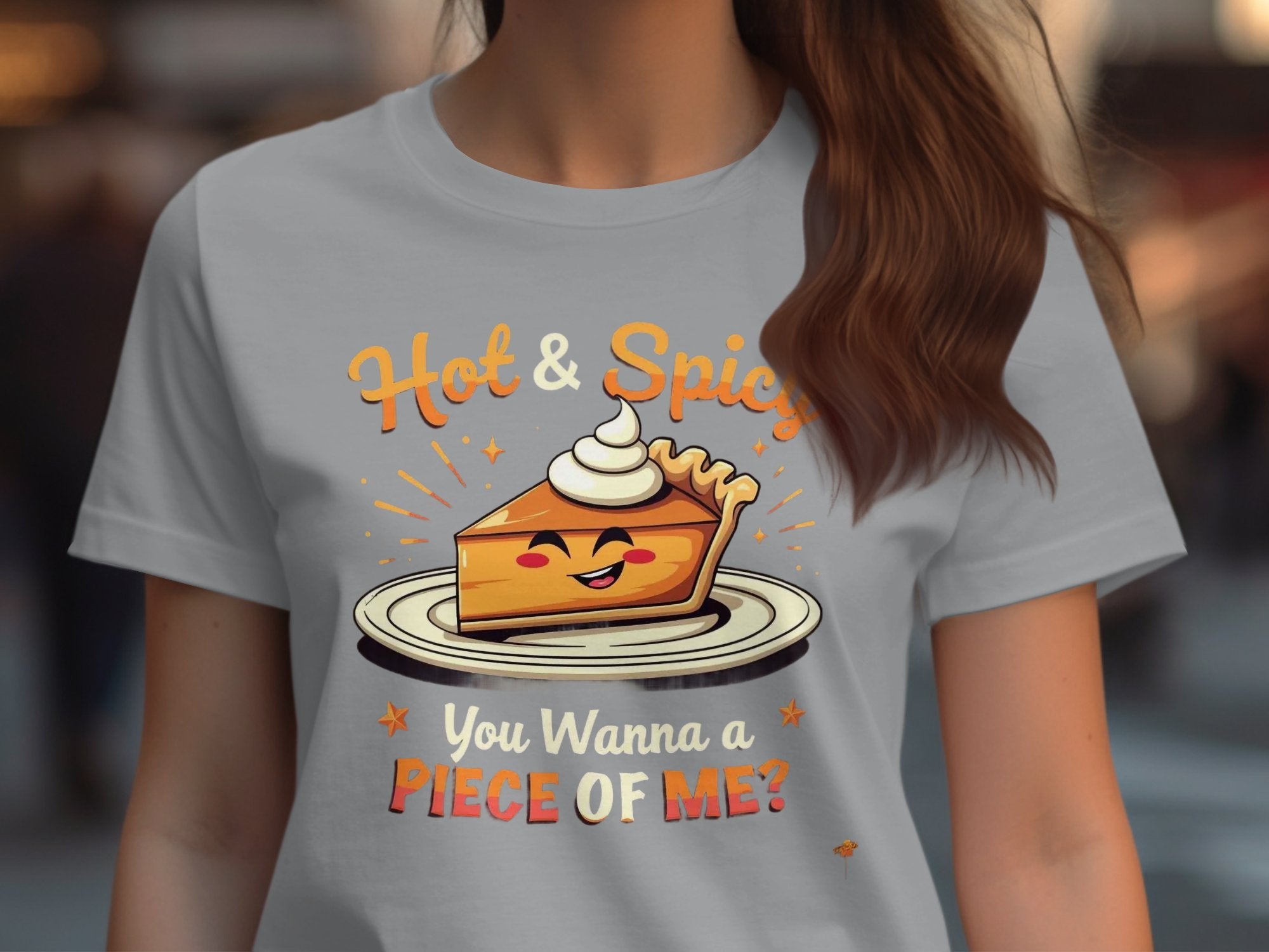 A woman wears a Garment Graphics gray t-shirt showcasing a pie slice with whipped cream. Hot & Spicy is above the image and You Wanna a Piece of Me? below. Ideal for casual outings, the background is creatively blurred.