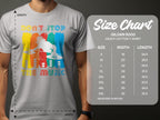 A person is wearing a Garment Graphics gray DJ T-shirt with Dont Stop The Music text, ideal for music lovers and party-goers. A Gildan 5000 size chart nearby displays sizes S to 5XL with their width and length measurements.