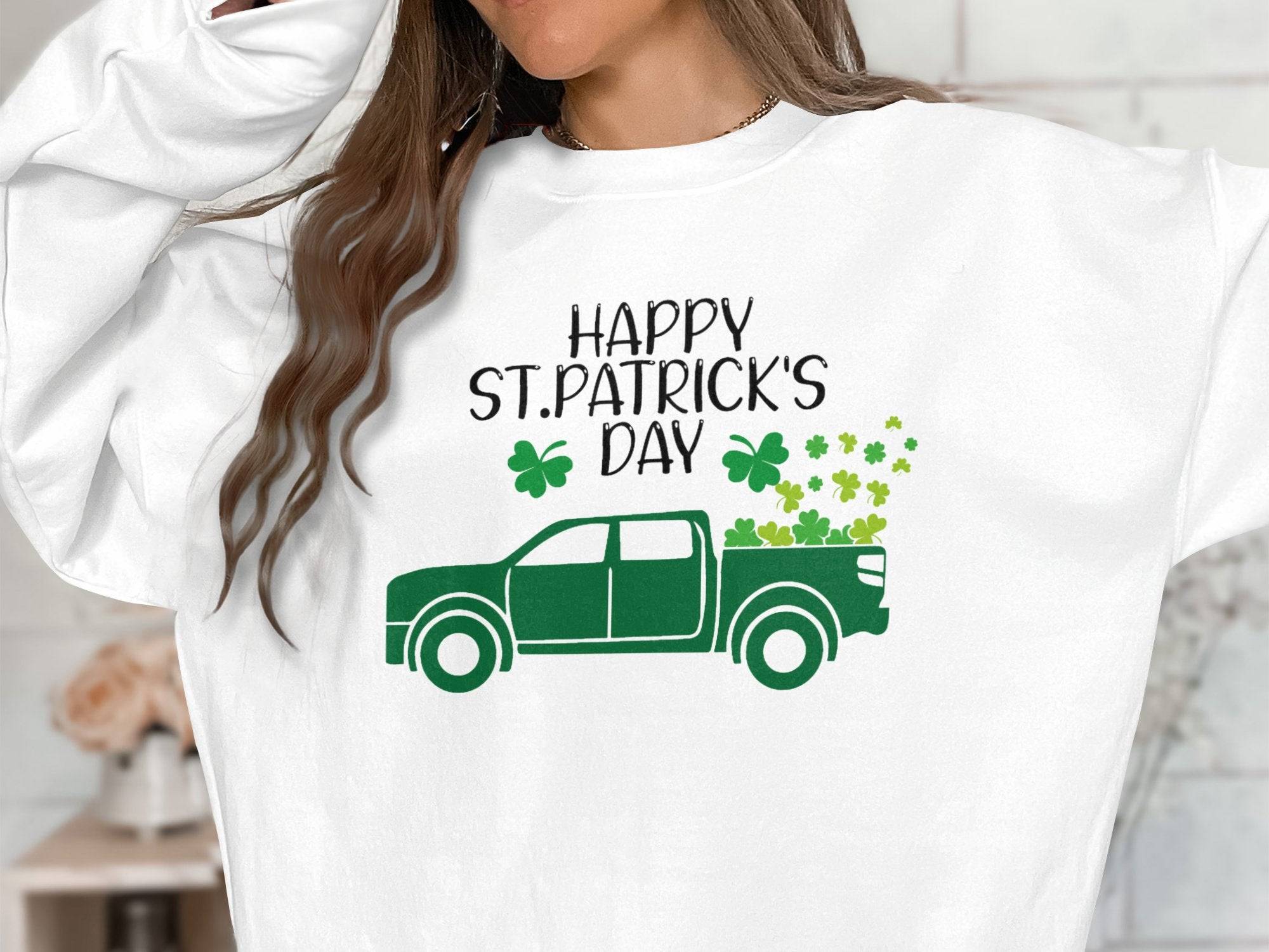 Someone is sporting a festive white Garment Graphics sweatshirt with a green truck and shamrocks. The words Happy St. Patricks Day enhance the cheerful vibe, though their face is not visible.