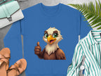 Garment Graphics offers a blue sweatshirt with a cheerful cartoon eagle design giving a thumbs-up, featuring large green eyes and a yellow beak. Displayed with a green striped shirt, sandals, watch, ferns, and purse on gray surface. Unisex sizing available for all.