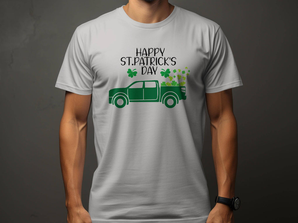 A person wears a Garment Graphics white t-shirt celebrating Irish pride, featuring a green pickup truck with shamrocks and Happy St. Patricks Day, set against a dark gray backdrop that enhances contrast, keeping the face hidden.