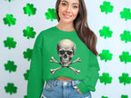A woman with long brown hair stands in front of a wall with green shamrocks, exuding an edgy style. Shes wearing a Garment Graphics unisex green sweatshirt featuring a skull and crossbones design, perfectly complemented by blue jeans.