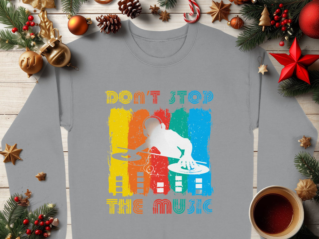 Garment Graphics offers a unisex gray shirt ideal for music enthusiasts, featuring a DJ silhouette with turntables set against vibrant orange, yellow, blue, and red vertical stripes. The shirt reads Dont Stop the Music and is styled with holiday decor and a cozy cup of coffee.