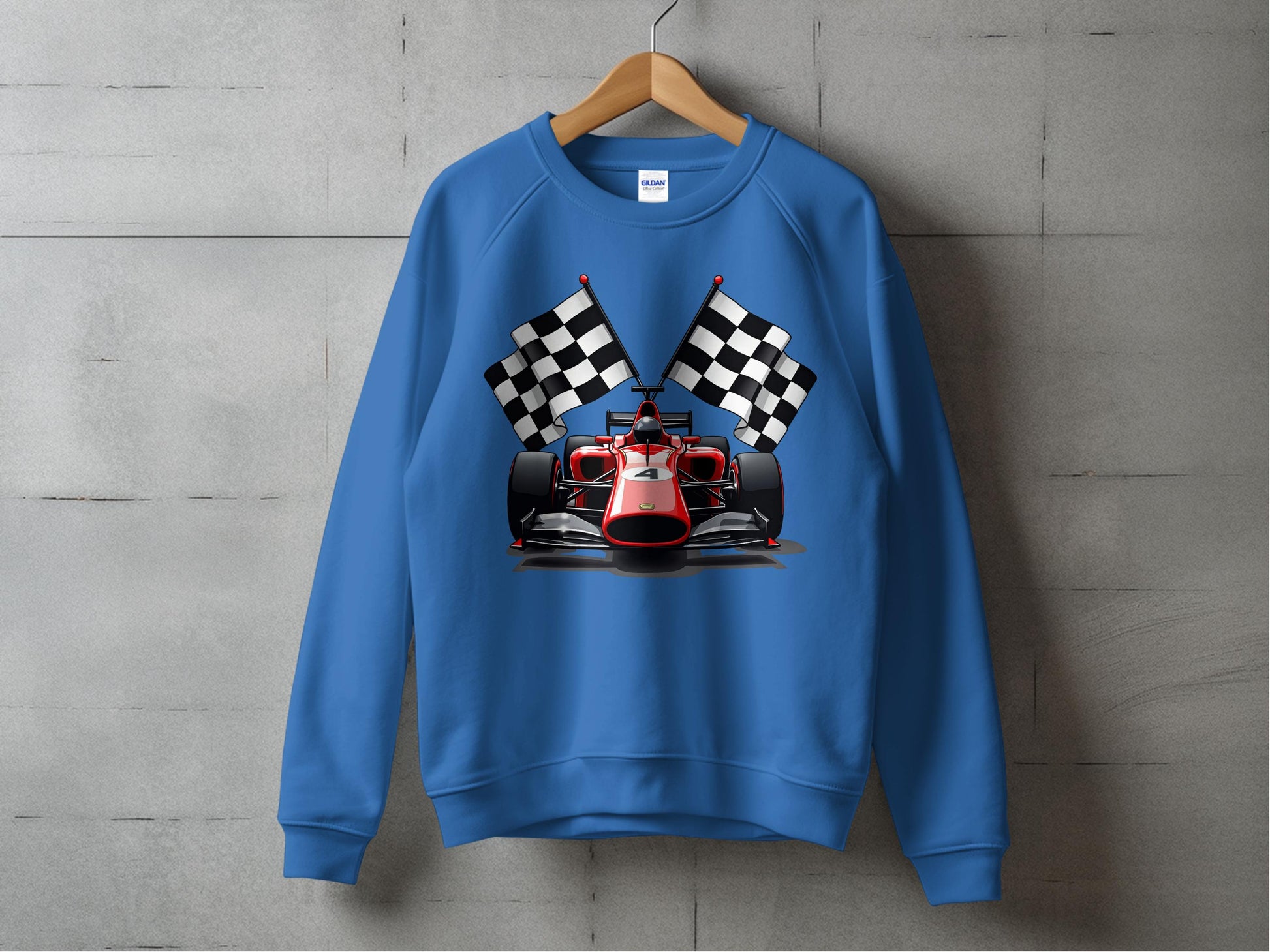 A Garment Graphics sweatshirt in blue features a red racing car with a driver and checkered flags, perfect for motorsport fans. Displayed on a wooden hanger, it stands out against a concrete wall background.