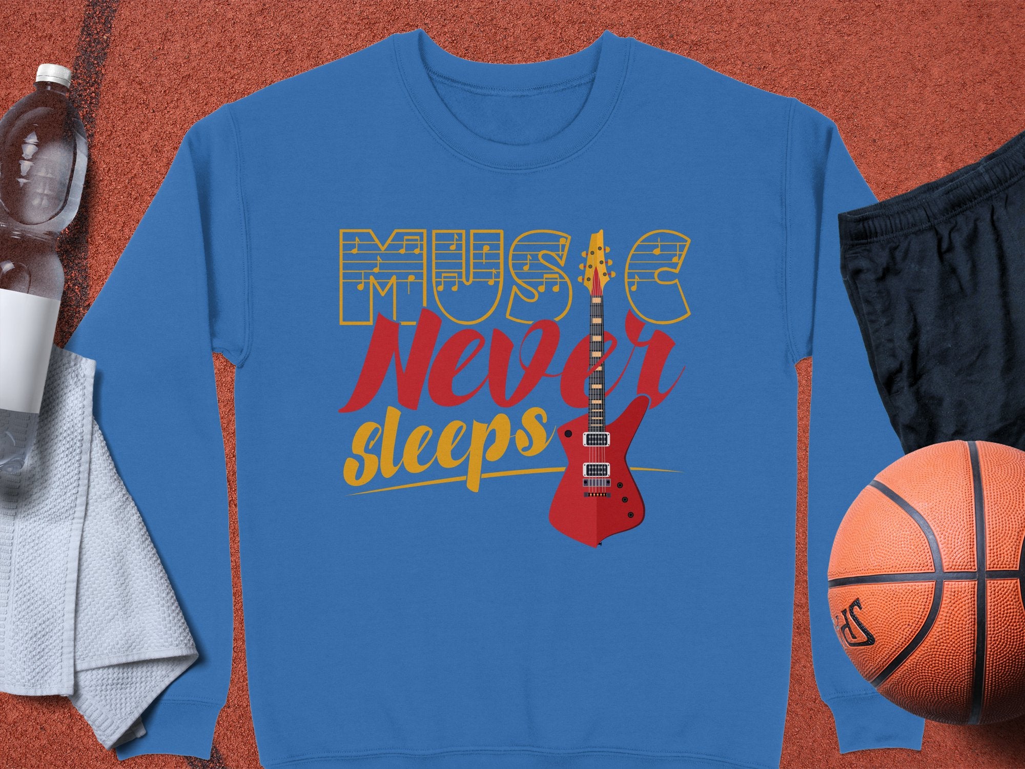 Garment Graphics offers a vibrant blue sweatshirt with Music Never Sleeps in gold and red, ideal for music lovers. Featuring a red electric guitar design, its styled with a basketball, black shorts, water bottle, and white towel on a textured background.