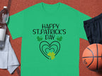 Garment Graphics T-shirt with HAPPY ST. PATRICKS DAY above a heart and shamrock adds festive flair, surrounded by a water bottle, towel, black shorts, and an orange basketball on a textured surface.