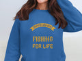 A person is wearing a Garment Graphics blue graphic sweatshirt with bold yellow text, Father and Son Fishing for Life. Their long brown hair cascades over the light beige couch in the background.