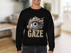 A person wears a black Garment Graphics sweatshirt with an elaborate eye design and GAZE text. Its unisex-sized, photographed against a blurred indoor backdrop.