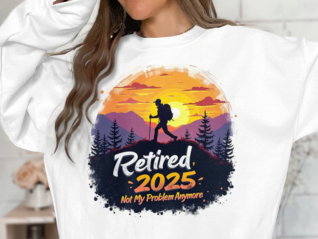 A person wears a white Garment Graphics unisex retirement sweatshirt with a hiker design, showing a hiker before a sunset, mountains, and trees. Text: Retired 2025 Not My Problem Anymore.