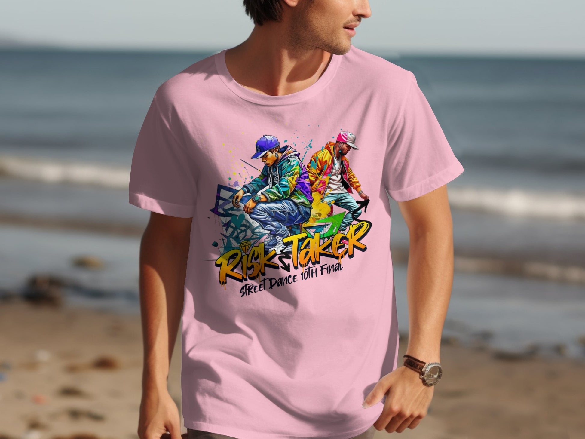 A person sports a Garment Graphics pink t-shirt showcasing an artistic design of two dancers, one blue and the other pink, alongside the phrases Risk Taker and Street Dance with Flava, creating a dynamic nod to street dance culture against the ocean backdrop.