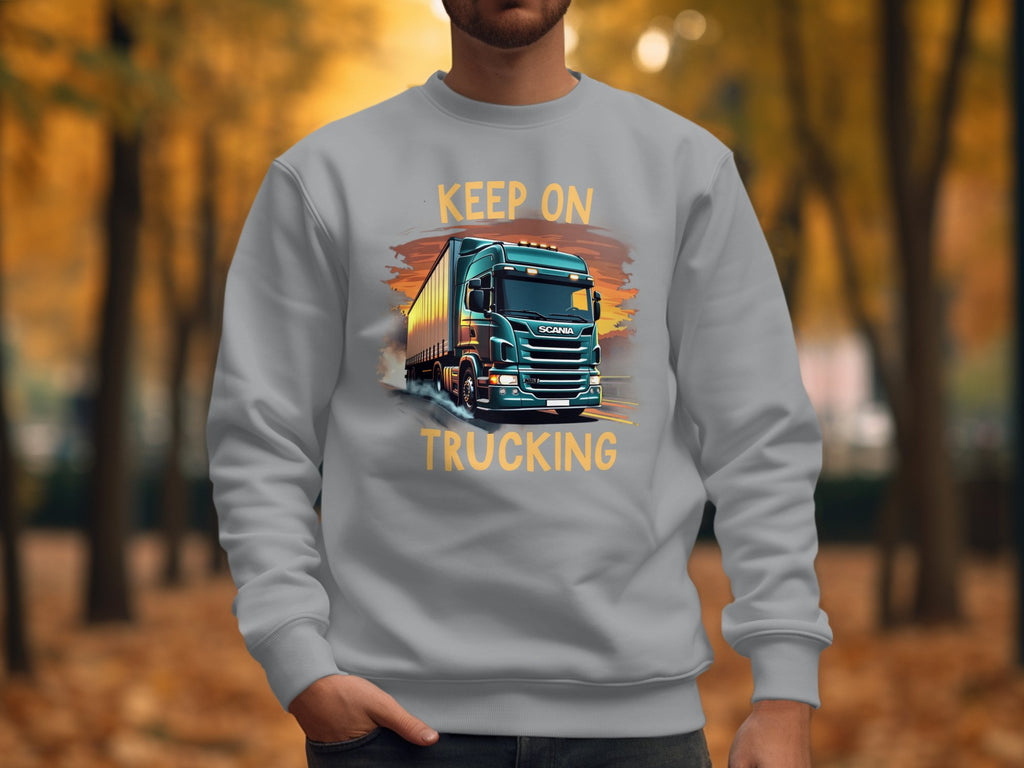 Someone sporting a Garment Graphics gray sweatshirt with a standout truck design and Keep On Trucking text, set against an autumn backdrop of trees and fallen leaves, enhancing the sweatshirts vibe.