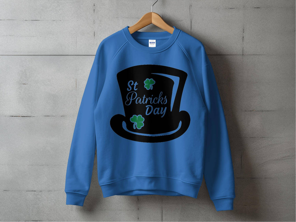 The Garment Graphics blue sweatshirt features a black top hat graphic with green clovers and St. Patricks Day text. Displayed on a wooden hanger against a concrete wall, it embodies festive charm for your celebrations.