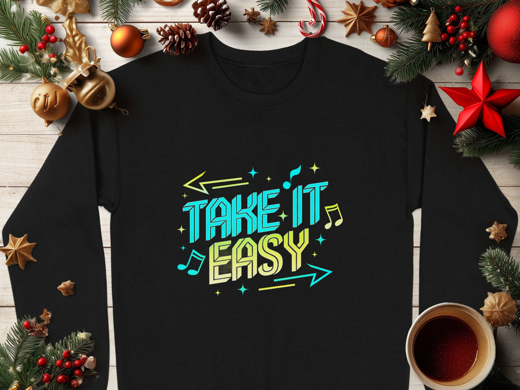 Garment Graphics offers a comfy black unisex sweatshirt featuring Take It Easy in vibrant blue and yellow. Musical notes, arrows, pine branches, ornaments, and a mug enhance the design on a wooden surface for a casual and relaxed vibe.