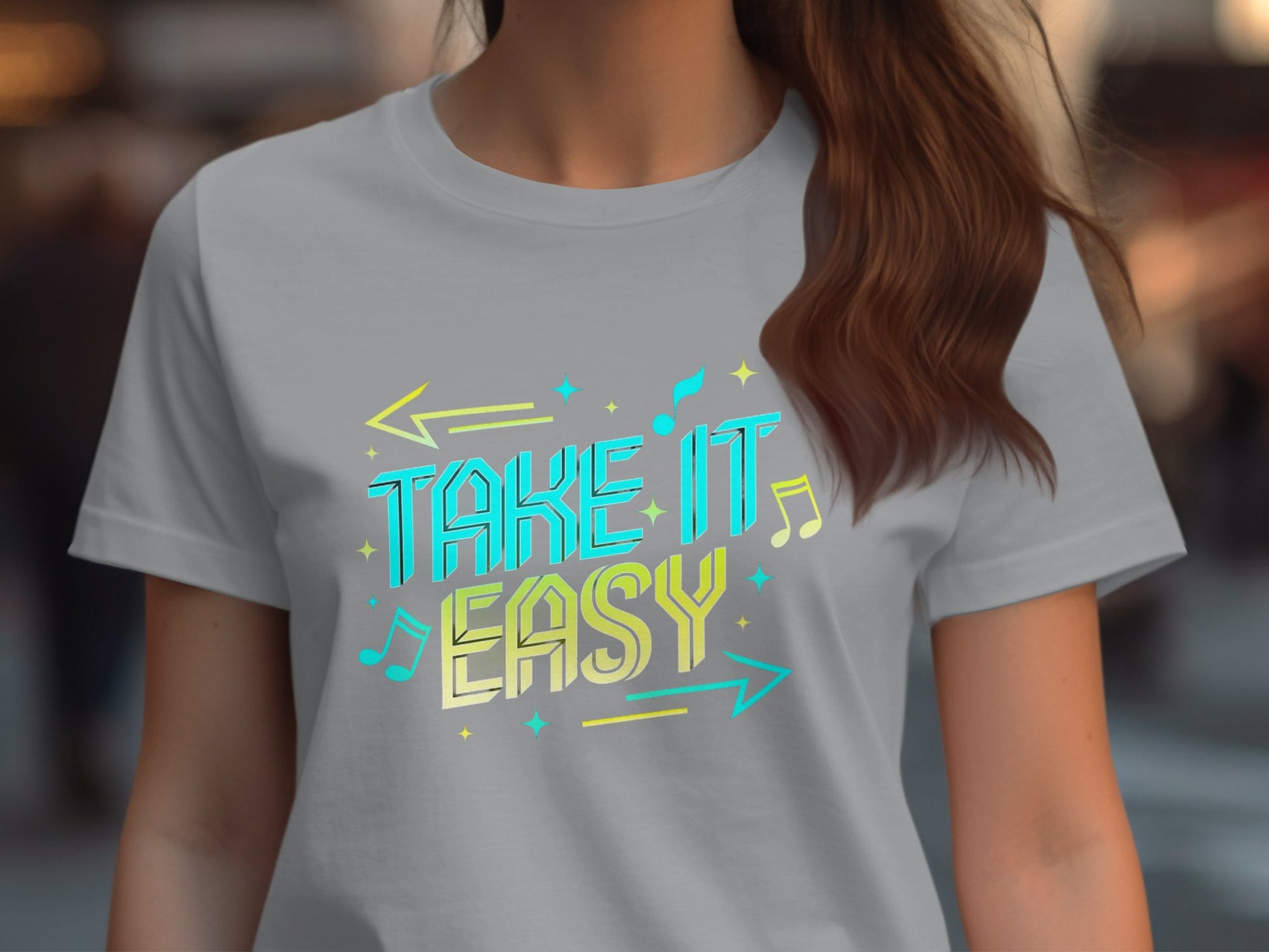 A person is wearing a Garment Graphics light gray T-shirt featuring the phrase Take It Easy in bright blue and yellow, accented by musical notes and arrows. The vibrant graphics enhance its trendy appeal against a blurred background.