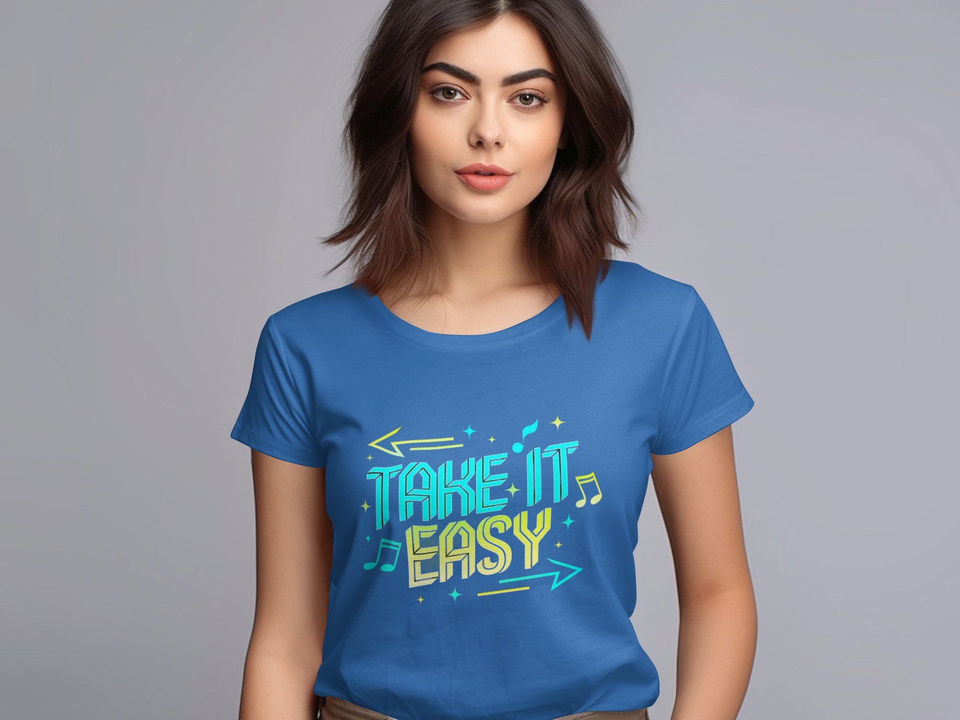 A person with medium-length brown hair is wearing a blue Garment Graphics Take It Easy T-Shirt adorned with vibrant graphics in a colorful, stylized font. The plain gray background complements the shirts stylish design.