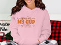 Wearing a cozy pink Youre my cup of tea hoodie by Garment Graphics, a person relaxes in a room decorated with a checkered pillow and blanket in the background.