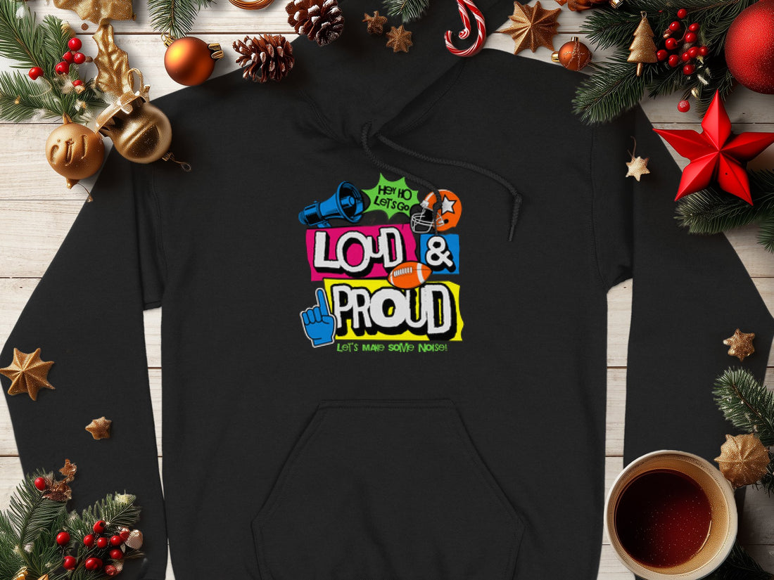 The Lets Make Some Noise hoodie by Garment Graphics showcases vibrant slogans like Hey Ho Lets Go and Loud & Proud, highlighted with microphone, star, and hand icons. Displayed on a wooden surface with Christmas decor and coffee, its ideal for adding festive flair to any moment.