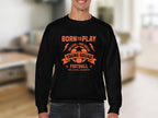 In a cozy room, someone wears Garment Graphics black football sweatshirt with orange text: Born to Play, One Goal - One Dream, Young Squad, Football, Kick, Score, Celebrate. Its ideal for young aspiring footballers and comes in unisex sizes.