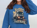 A person wears a blue Garment Graphics sweatshirt with a truck illustration on a road at sunset. Unisex sizing ensures comfort, with Keep On Trucking text completing this standout wardrobe piece.