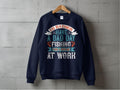 A Garment Graphics navy blue fishing sweatshirt hangs against a gray concrete wall, featuring colorful text: Id rather have a bad day fishing than a good day at work. Ideal for fishing enthusiasts, it comes in unisex sizing to fit all fans of the sport.