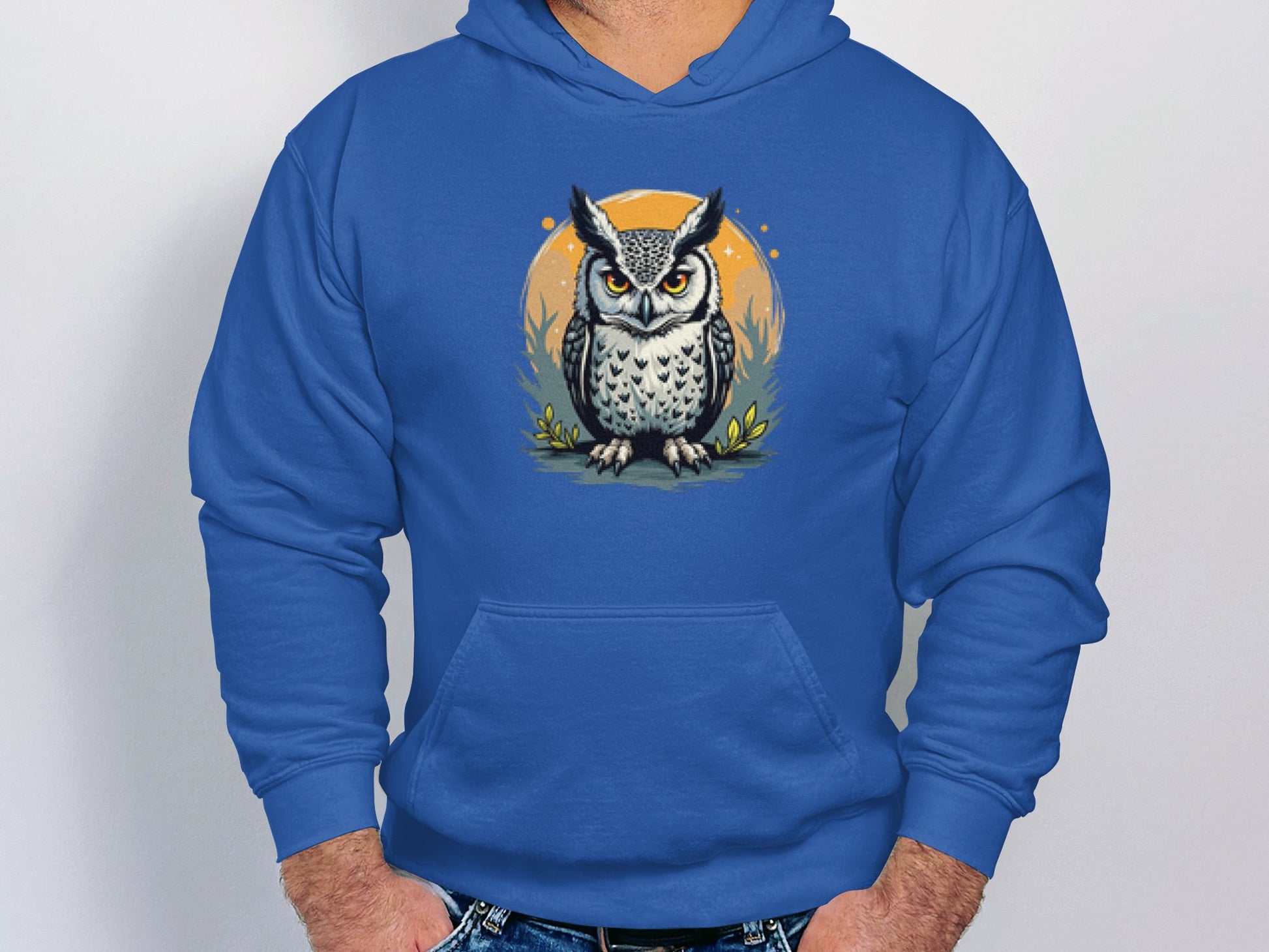 The Fierce Owl Illustration Hoodie by Garment Graphics features a bold owl design on an orange circle. Made from medium-heavy fabric, it has a cozy front pocket. A person can be seen tucking their hands into the pocket against a plain light background.