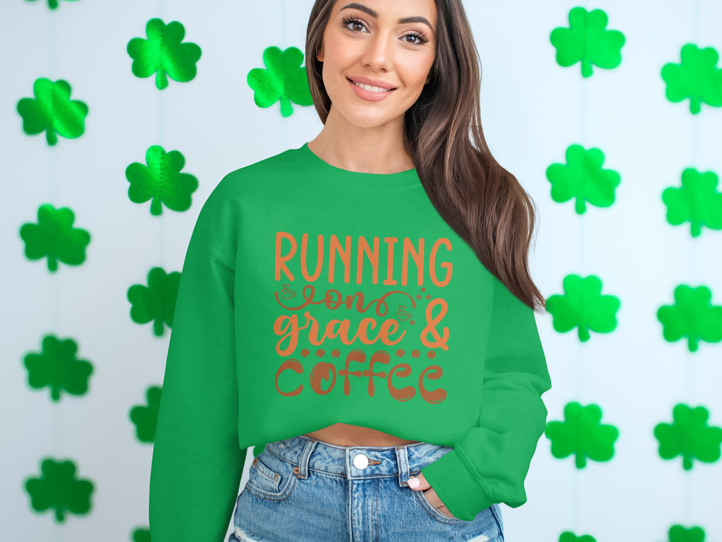 A person in a unisex Garment Graphics sweatshirt with Running on Grace & Coffee stands by a wall of green shamrock cutouts, perfectly paired with denim shorts.