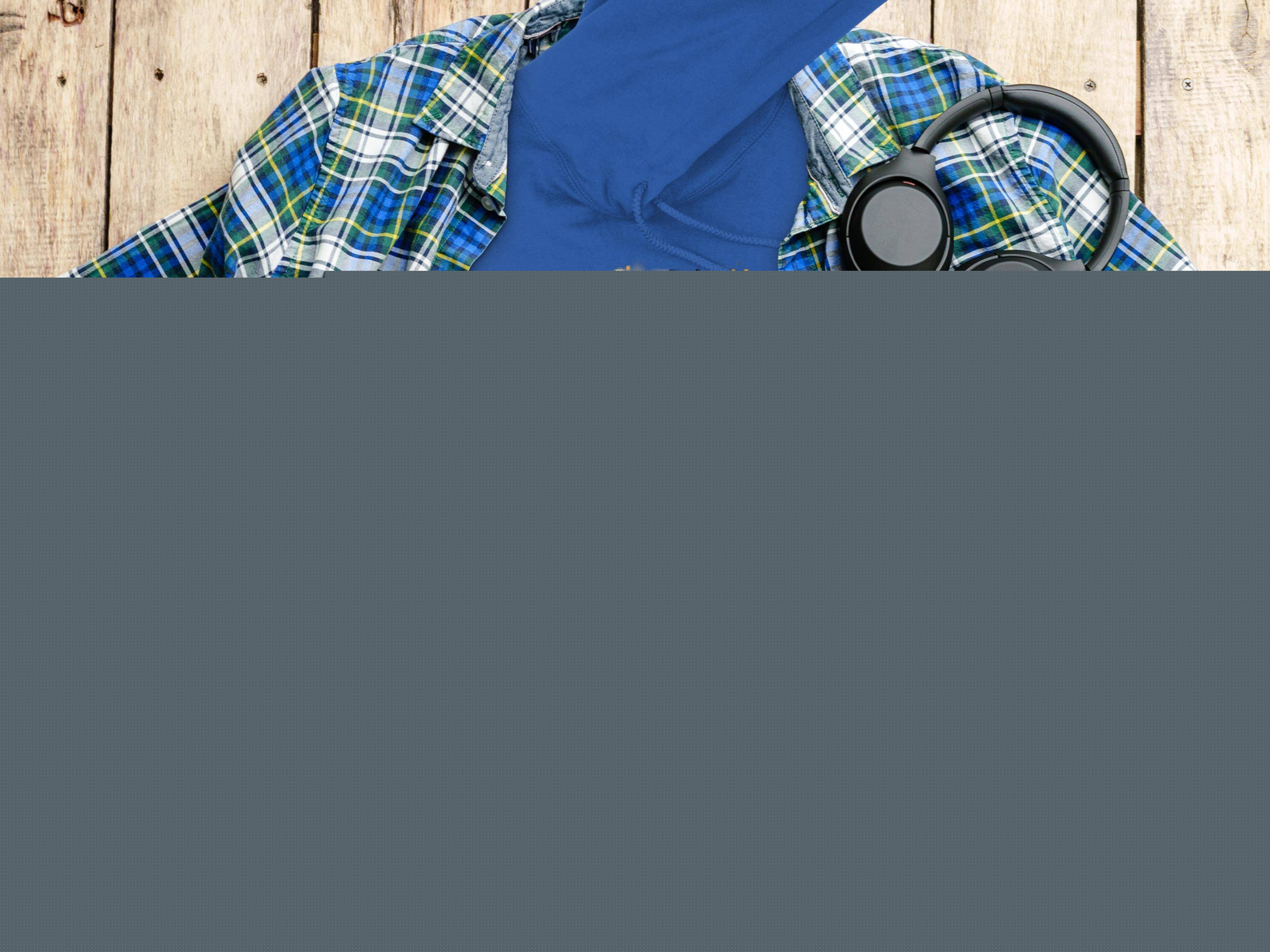 A flat lay displays a Garment Graphics Graphic Bulldog Design Hoodie with CITY KING text. Accompanying it are a plaid shirt, headphones, camera, water bottle, and coffee cup on a wooden surface.