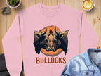 Garment Graphics presents this unisex pink sweatshirt with a striking design: two bulls facing on an orange circle, BULLOCKS printed below. Set amidst denim, a cappuccino, a plant, and a rock for artistic flair.