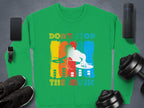 A dynamic DJ-themed green sweatshirt from Garment Graphics features Dont Stop the Music text. On a gray backdrop, it is paired with a smartphone, wireless speaker, smartwatch, sneakers, and weights—ideal for stylish music enthusiasts craving rhythm.