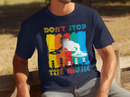 A person wears a Garment Graphics navy T-shirt with a DJ silhouette and colorful stripes. The text reads Dont Stop the Music. They sit on an outdoor wooden bench, ideal for music lovers.