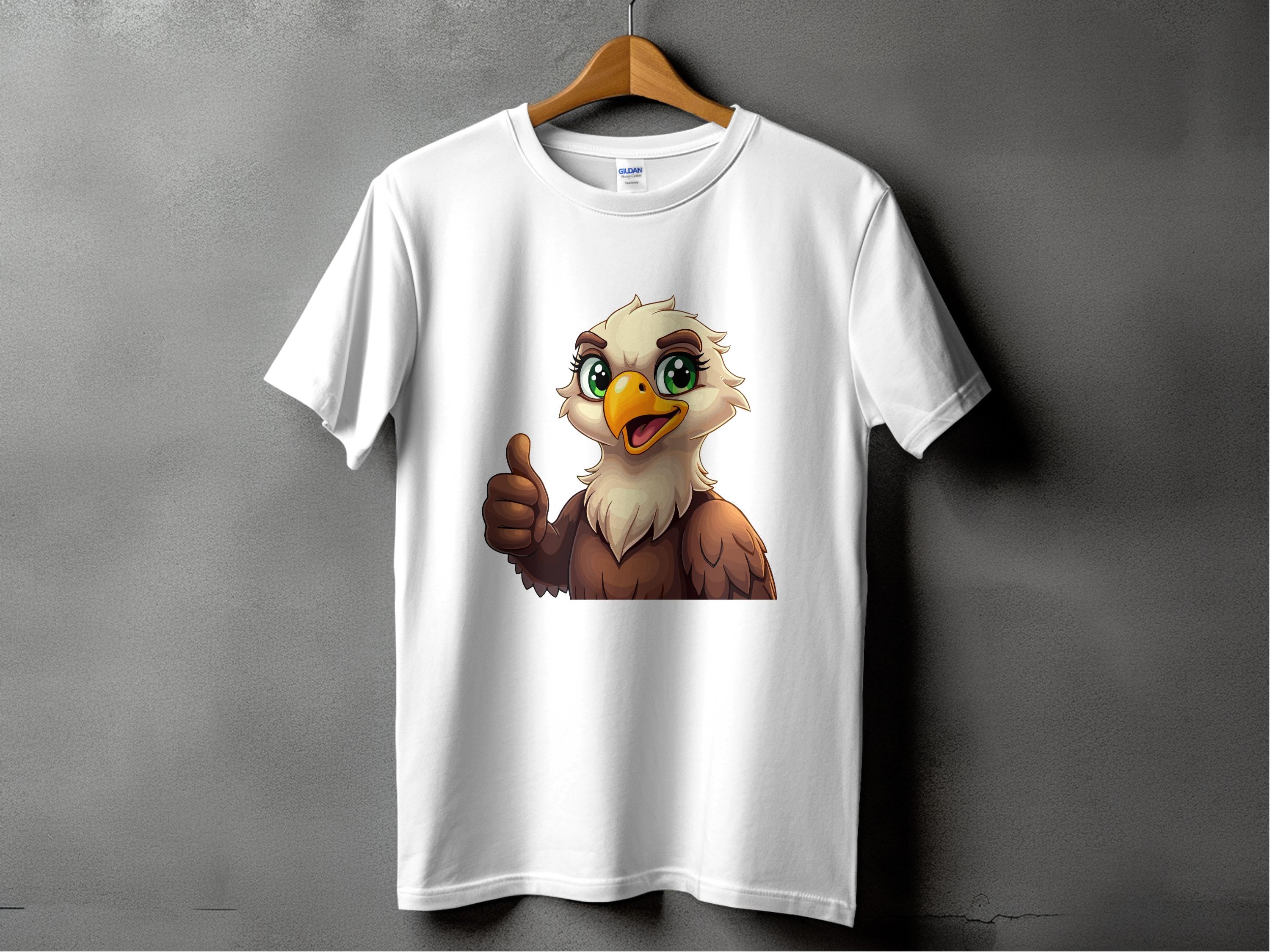 A Garment Graphics classic fit T-shirt hangs on a wooden hanger, featuring a cartoon eagle with large green eyes and a thumbs-up. This fun wardrobe staple pops against the solid gray wall.