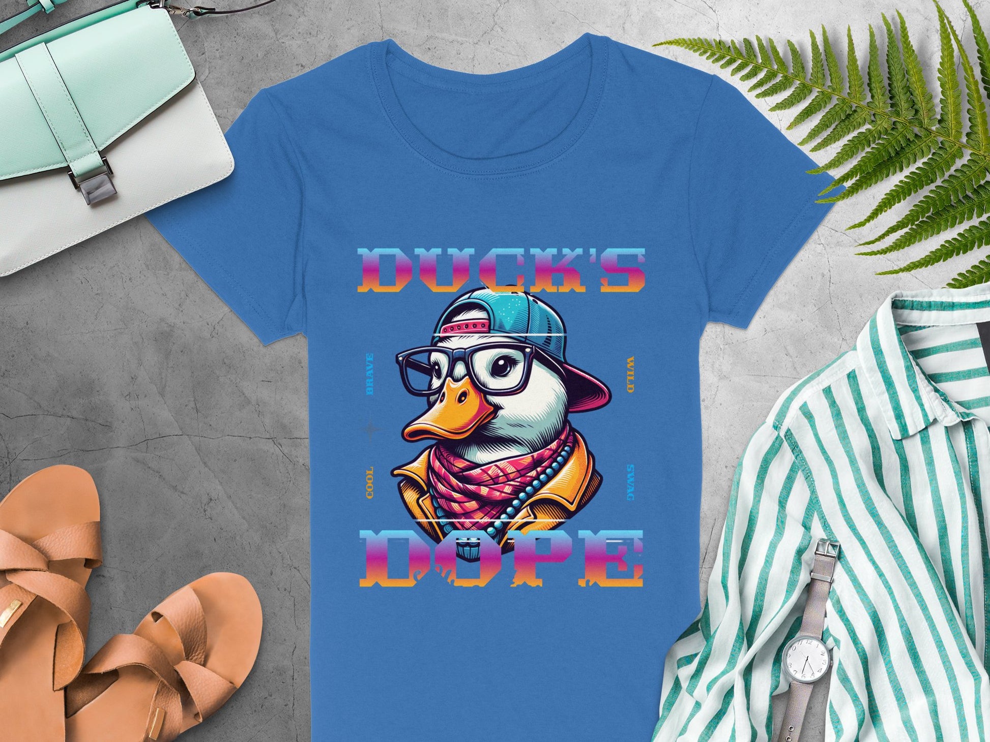 Garment Graphics blue tee showcases a duck in a cap, glasses, and jacket with Ducks Dope text. Styled with sandals, purse, striped shirt, watch, and fern leaves on gray—ideal for those who love unique T-shirts.