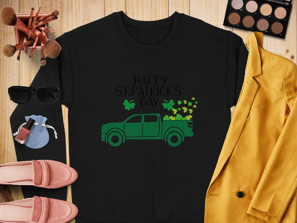 The Garment Graphics festive sweatshirt showcases a green truck and shamrocks with Happy St. Patricks Day, displayed on wood with a yellow blazer, pink shoes, sunglasses, makeup palette, brushes, and a pouch.