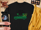 The Garment Graphics festive sweatshirt showcases a green truck and shamrocks with Happy St. Patricks Day, displayed on wood with a yellow blazer, pink shoes, sunglasses, makeup palette, brushes, and a pouch.