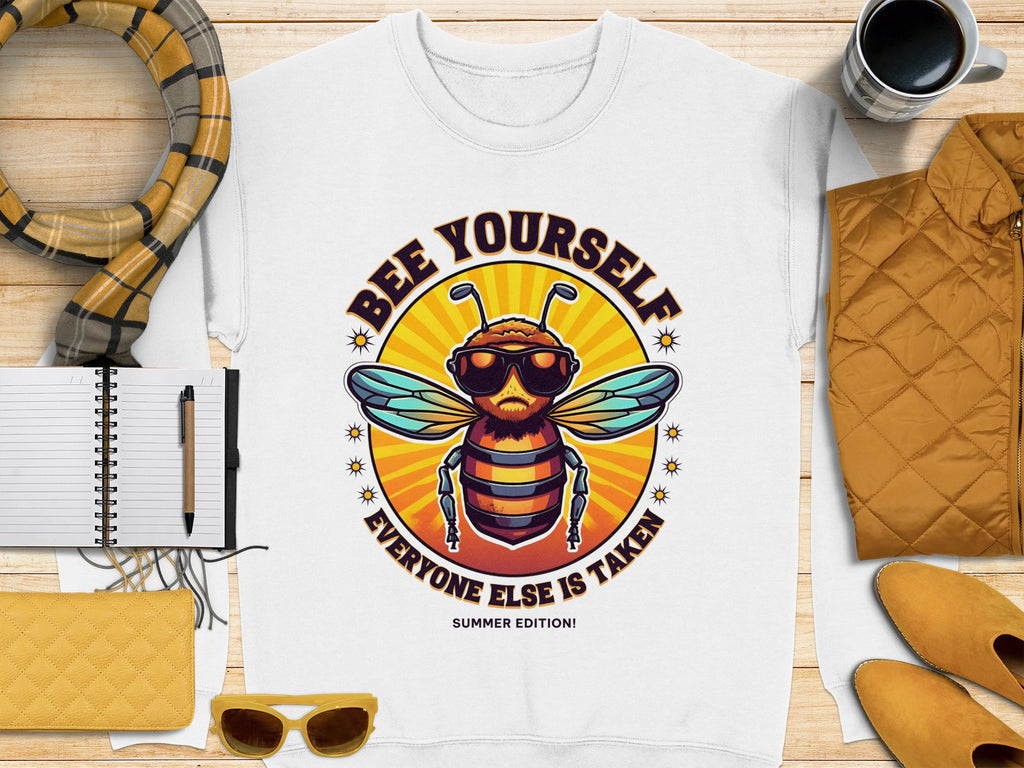 A white unisex Garment Graphics T-shirt with a bee in sunglasses and Bee Yourself Everyone Else is Taken text pairs perfectly with essentials like a notebook, scarf, and yellow quilted jacket for embracing your unique style.