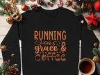 Garment Graphics black graphic sweatshirt features Running on grace & coffee in brown text with cup illustrations, surrounded by pine branches, ornaments, and a coffee cup on white wood. It exudes cozy vibes and is available in unisex sizes.
