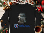 A black Garment Graphics crewneck sweatshirt, featuring a detailed Scania truck illustration and the griffin logo, lies on a wooden surface. Ideal for truck enthusiasts, its surrounded by festive decorations: pine branches, ornaments, and a cup of coffee.