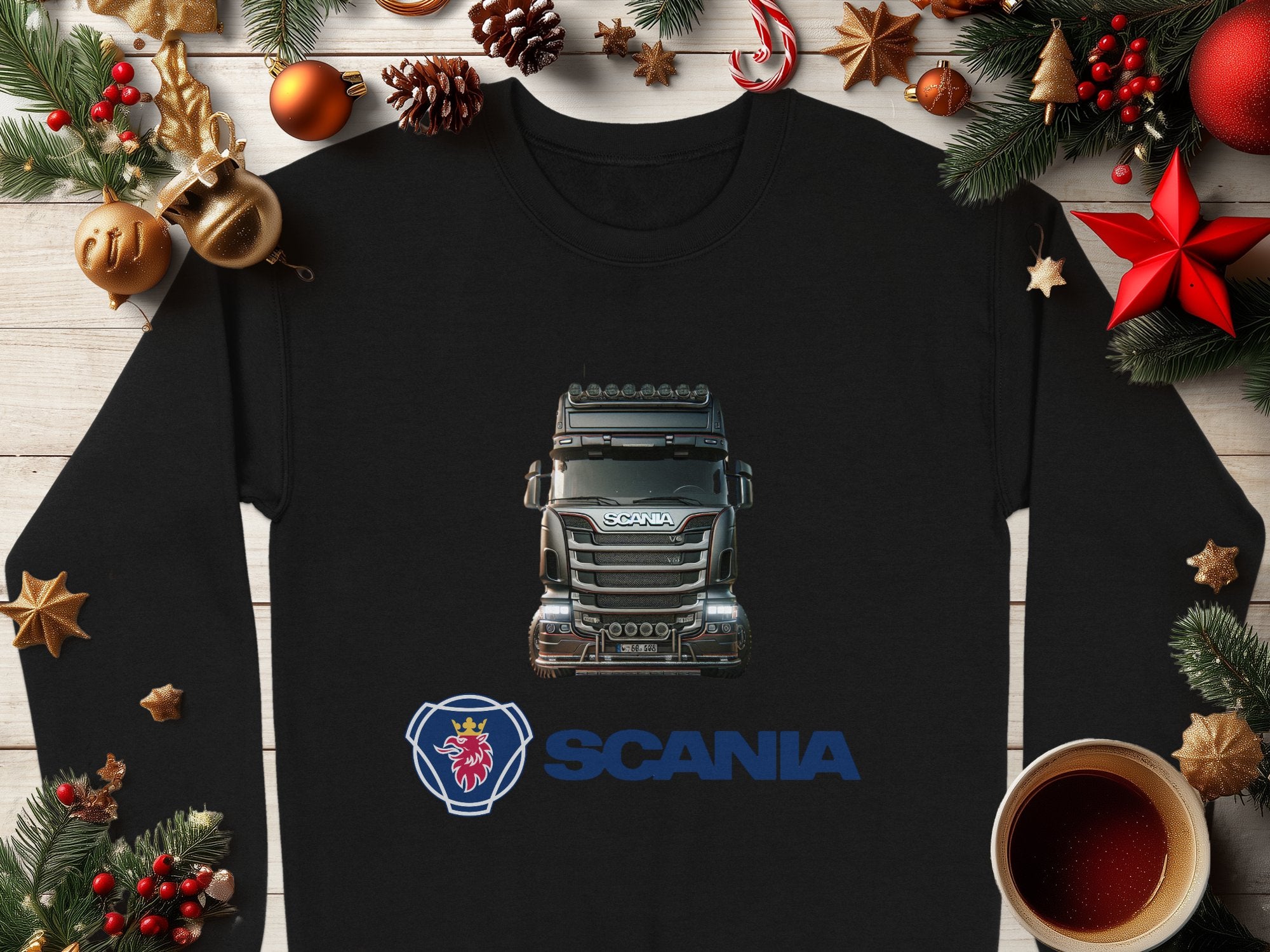 A black Garment Graphics crewneck sweatshirt, featuring a detailed Scania truck illustration and the griffin logo, lies on a wooden surface. Ideal for truck enthusiasts, its surrounded by festive decorations: pine branches, ornaments, and a cup of coffee.