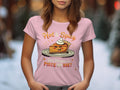 A woman wears a pink Garment Graphics T-shirt with a cartoon spicy pie and texts Hot & Spicy and You Wanna a Piece of Me?. The soft-focus snowy tree backdrop makes it ideal for casual outings.