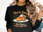 A person with long wavy hair is wearing a stylish Garment Graphics sweatshirt featuring a smiling slice of pie topped with whipped cream. Above, it says Hot & Spicy, and below, You Wanna a Piece of Me? This unisex piece is perfect for fans of bold, playful fashion.