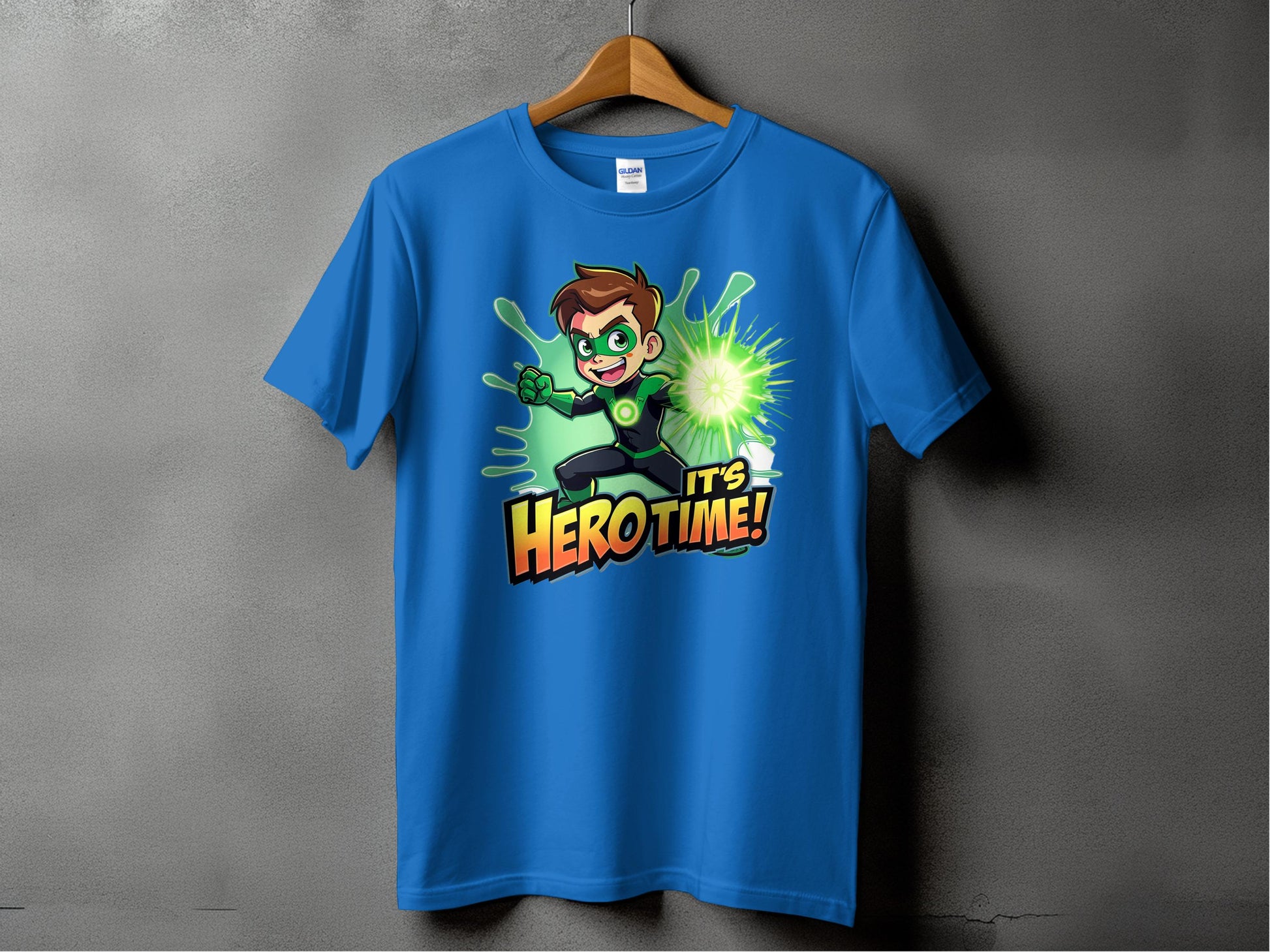 A vibrant blue Garment Graphics t-shirt on a wooden hanger against a gray wall features a superhero cartoon character in a green suit with a glowing hand and the text Its Hero Time! Available in family sizing for heroic style for everyone.