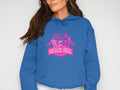 A person in a vibrant Garment Graphics Always Party Beach Girl Hoodie displays its pink graphic of three women in swimwear and palm trees, with long dark hair accentuating the casual look against a plain backdrop.