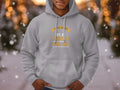 A fishing enthusiast proudly wears his favorite Garment Graphics gray hoodie, featuring Father and Son Fishing Partners for Life, while standing in a snowy, warmly lit outdoor setting.