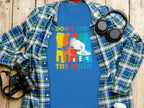 A Garment Graphics blue t-shirt with a DJ graphic and Dont Stop the Music text lies on a wooden surface. Its ideal for music enthusiasts, accompanied by a plaid shirt, black headphones, a camera, and a white reusable water bottle.